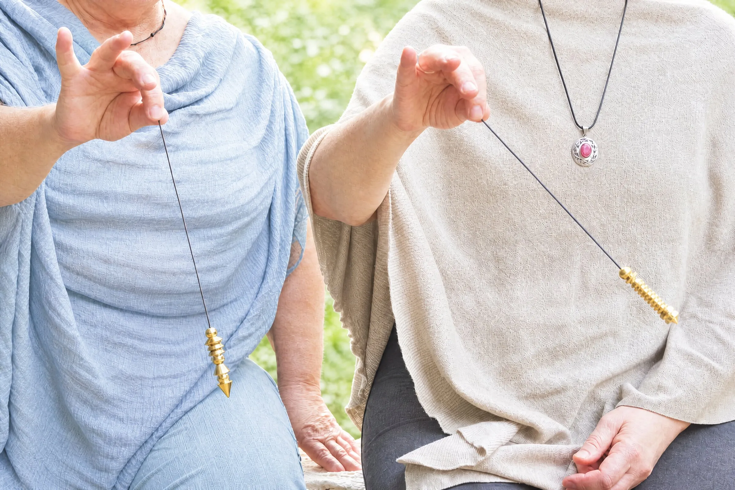 Dos personas practican al aire libre, cada una con su péndulo colgando de los dedos